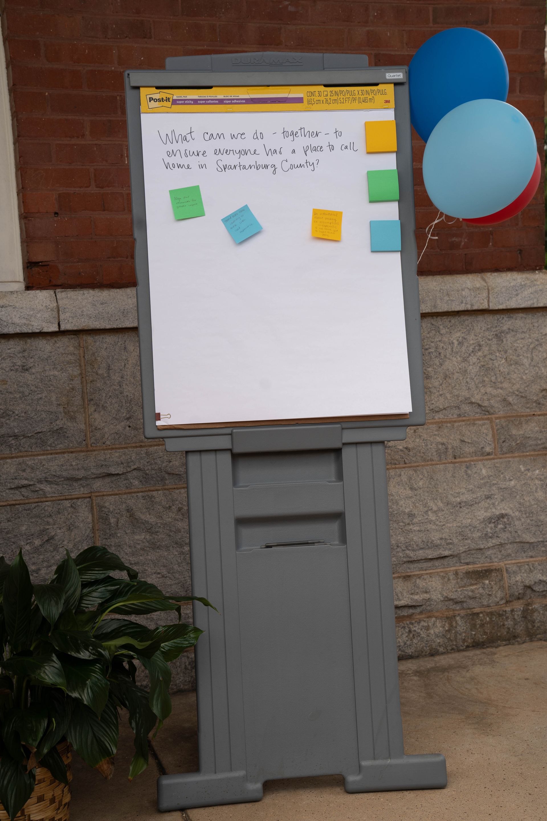 Gray easel with whiteboard and sticky notes, blue balloons in the background.