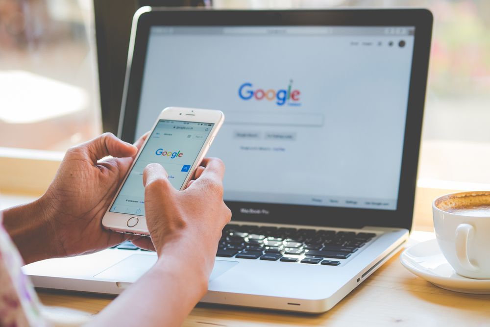 A person is using a cell phone in front of a laptop computer.