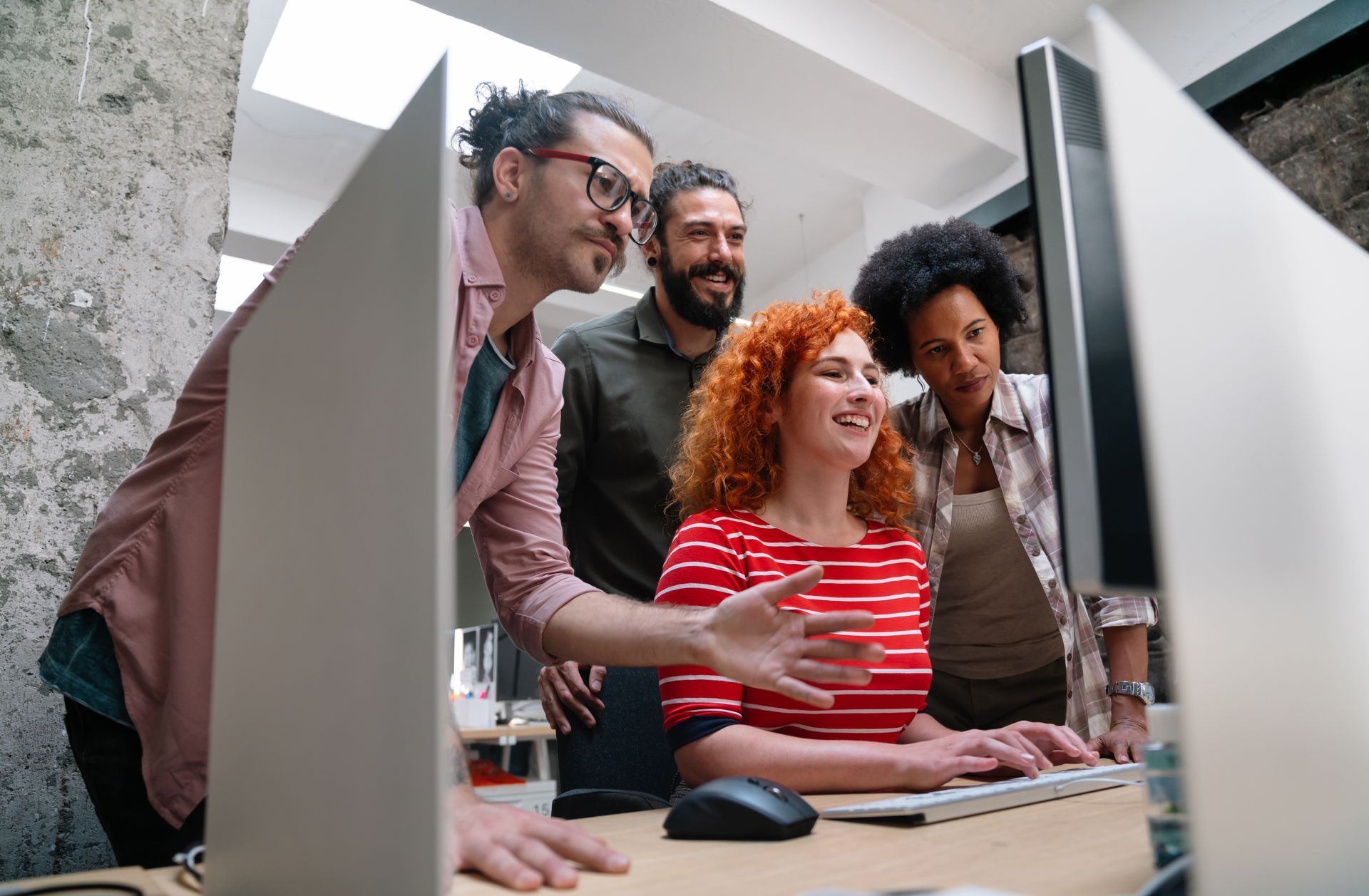 Coworkers smiling around a computer in an office, looking at the screen together