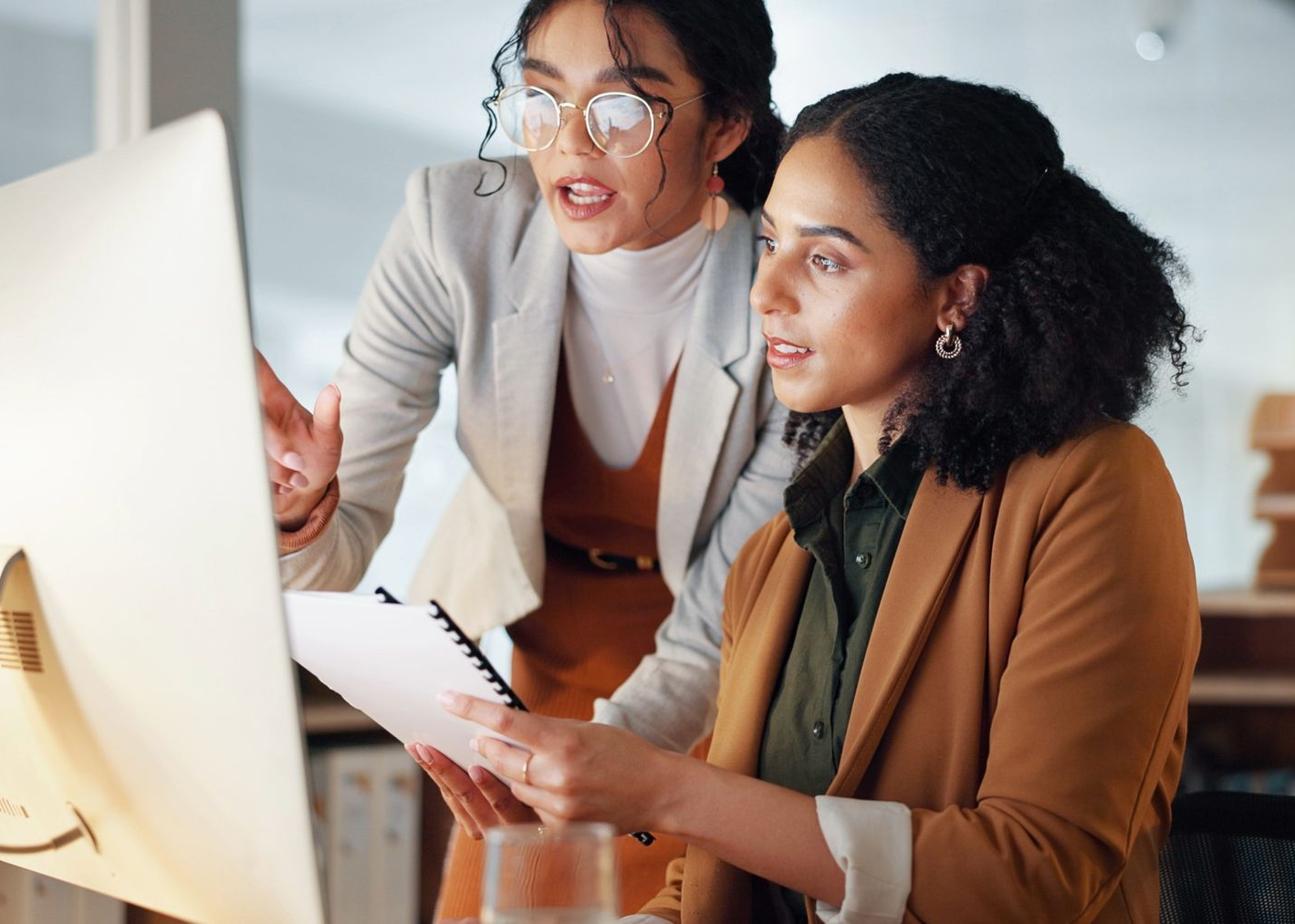 Two people reviewing paperwork and a computer screen in an office. One points, the other looks on.