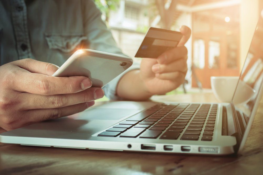 A person is holding a credit card and a cell phone while using a laptop computer.