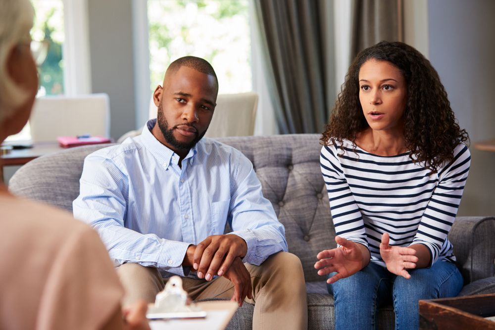A man and a woman are sitting on a couch talking to a therapist.