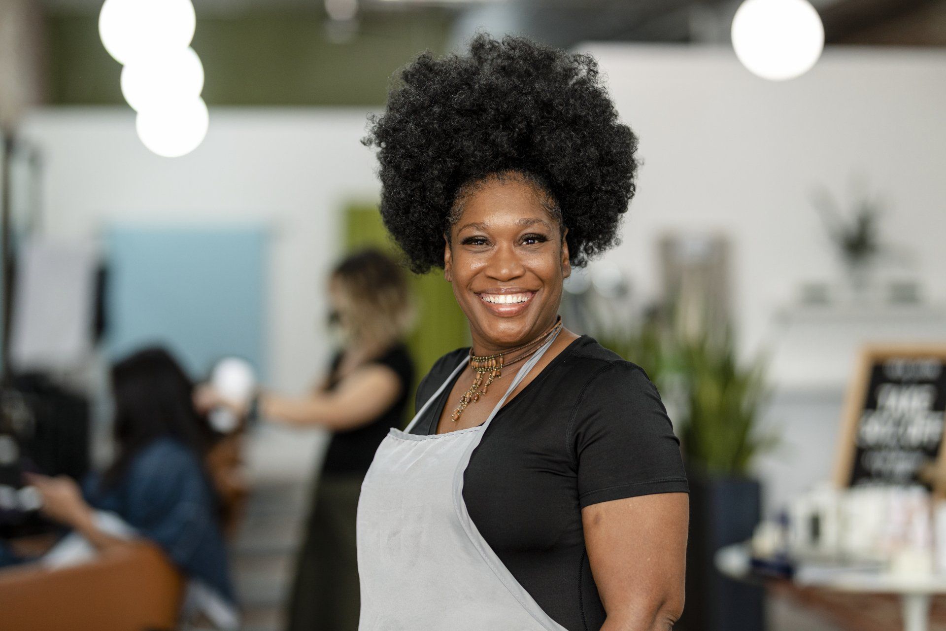 A woman in an apron is smiling in a salon.