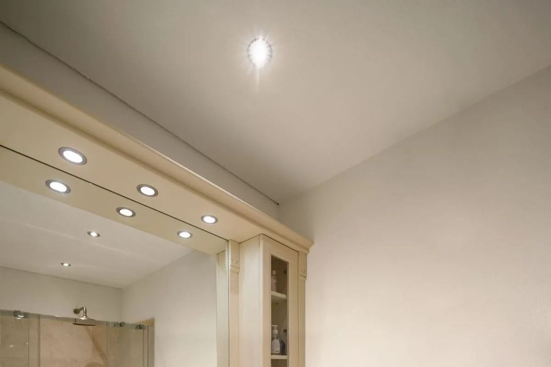 Beige interior with recessed ceiling lights and a doorway to a tiled bathroom