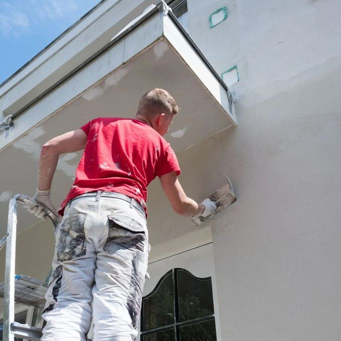 Worker in red shirt plastering the exterior wall of a building on a ladder