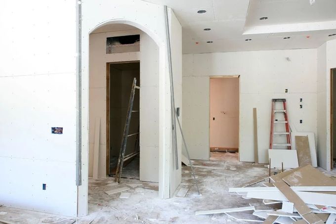 Unfinished interior with drywall debris, ladders, and open doorways during renovation