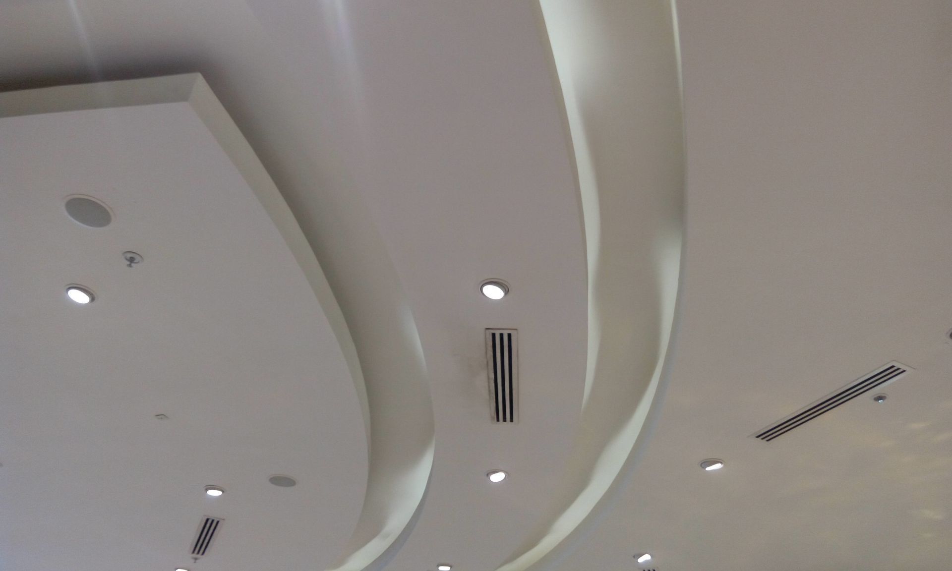 Ceiling with curved white panels, recessed lights, and air vents in a modern interior.