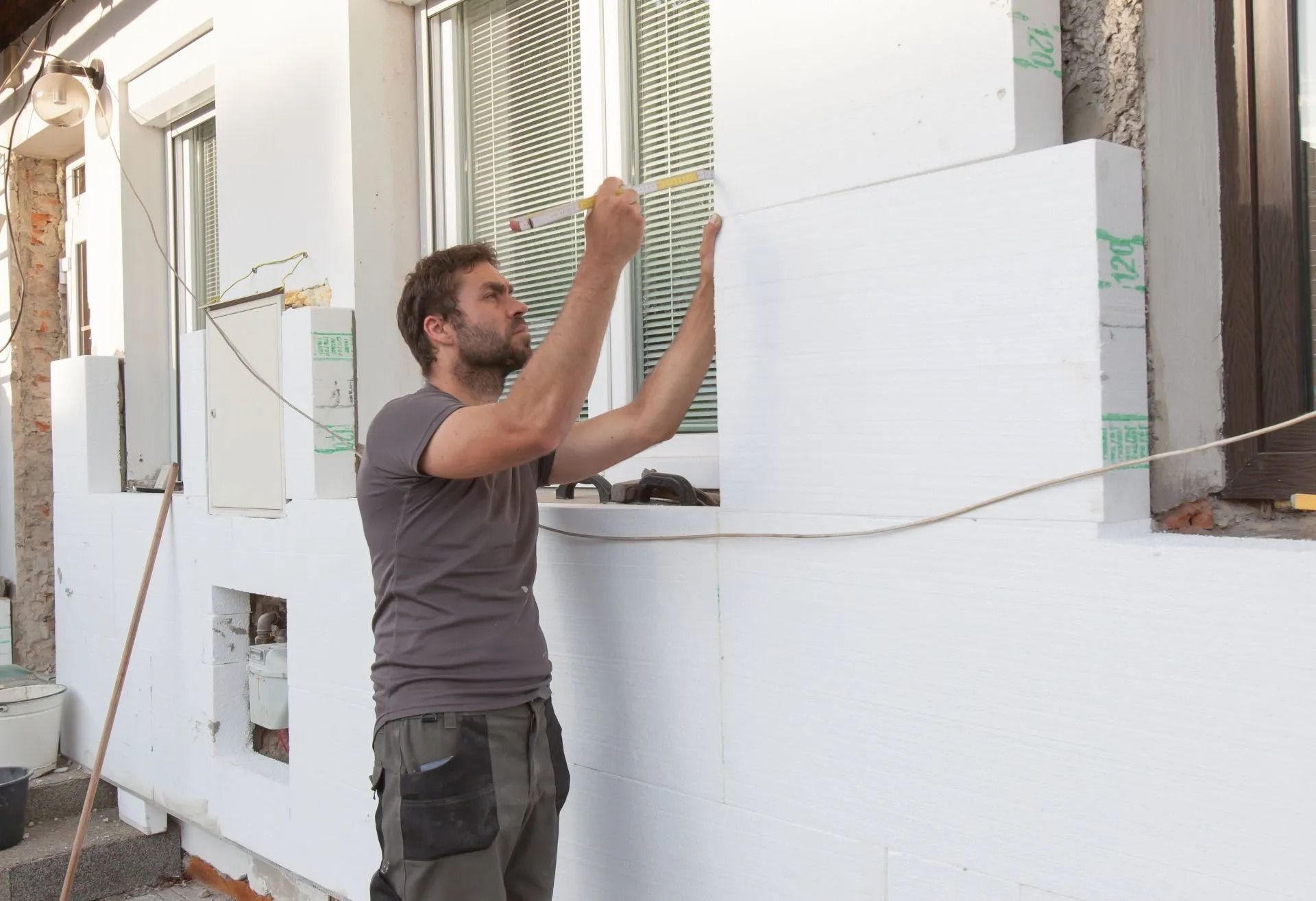 Man installing white foam insulation panels on an exterior wall of a house