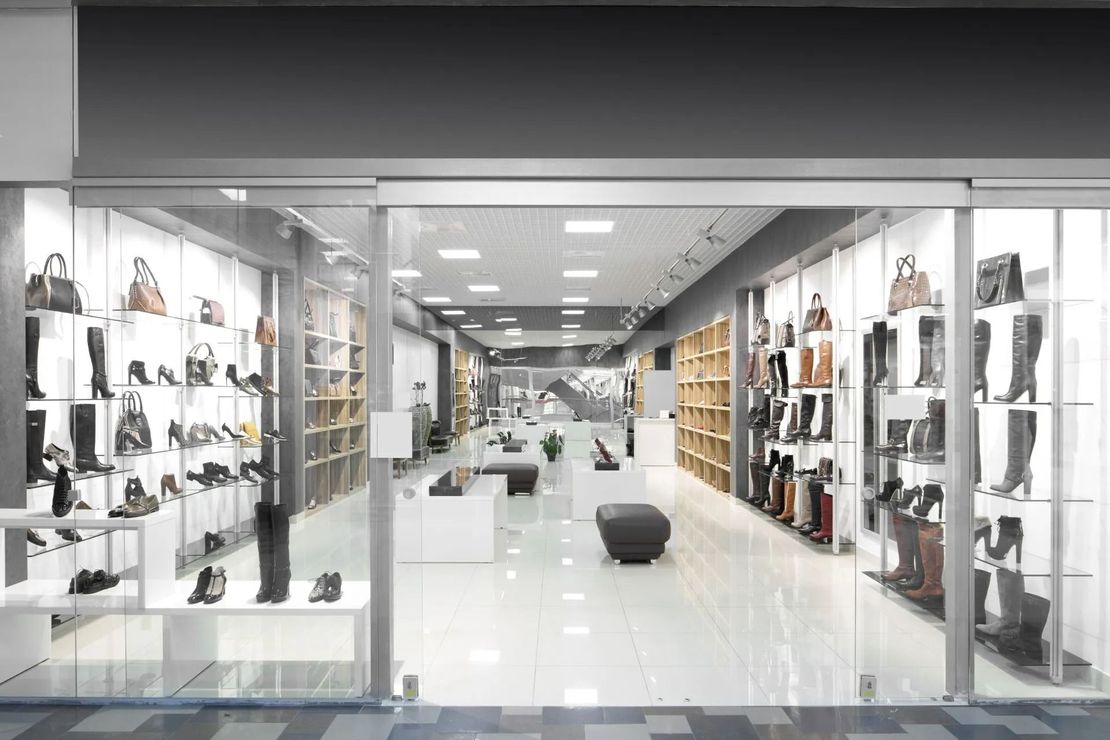 Modern shoe store interior with glass displays and white floor, shelves of boots and handbags lining both sides