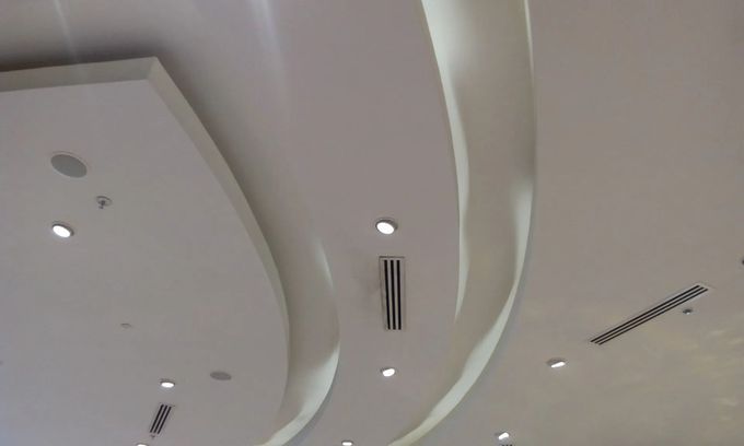 Ceiling with curved white panels, recessed lights, and air vents in a modern interior.