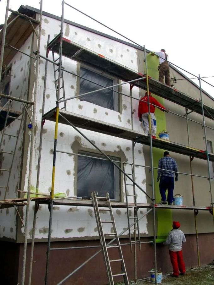 Workers on scaffolding applying exterior insulation to a house facade