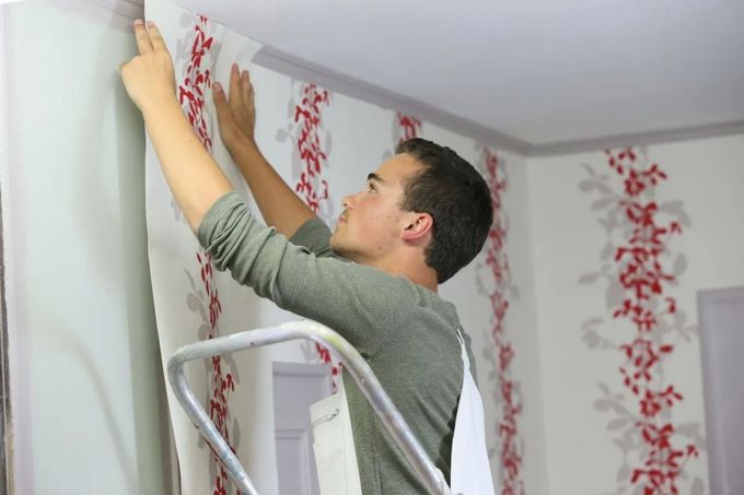 Person on a ladder hanging red floral wallpaper in a room