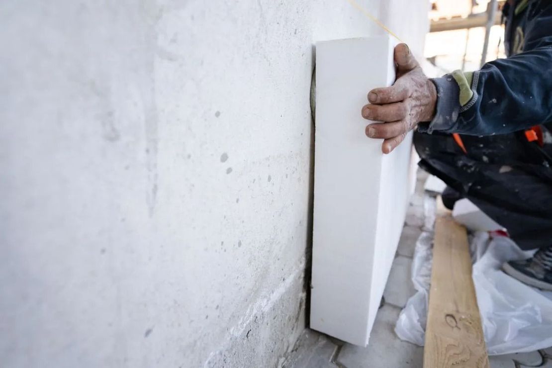 Hand installing a white wall panel beside a rough plaster wall in an unfinished room