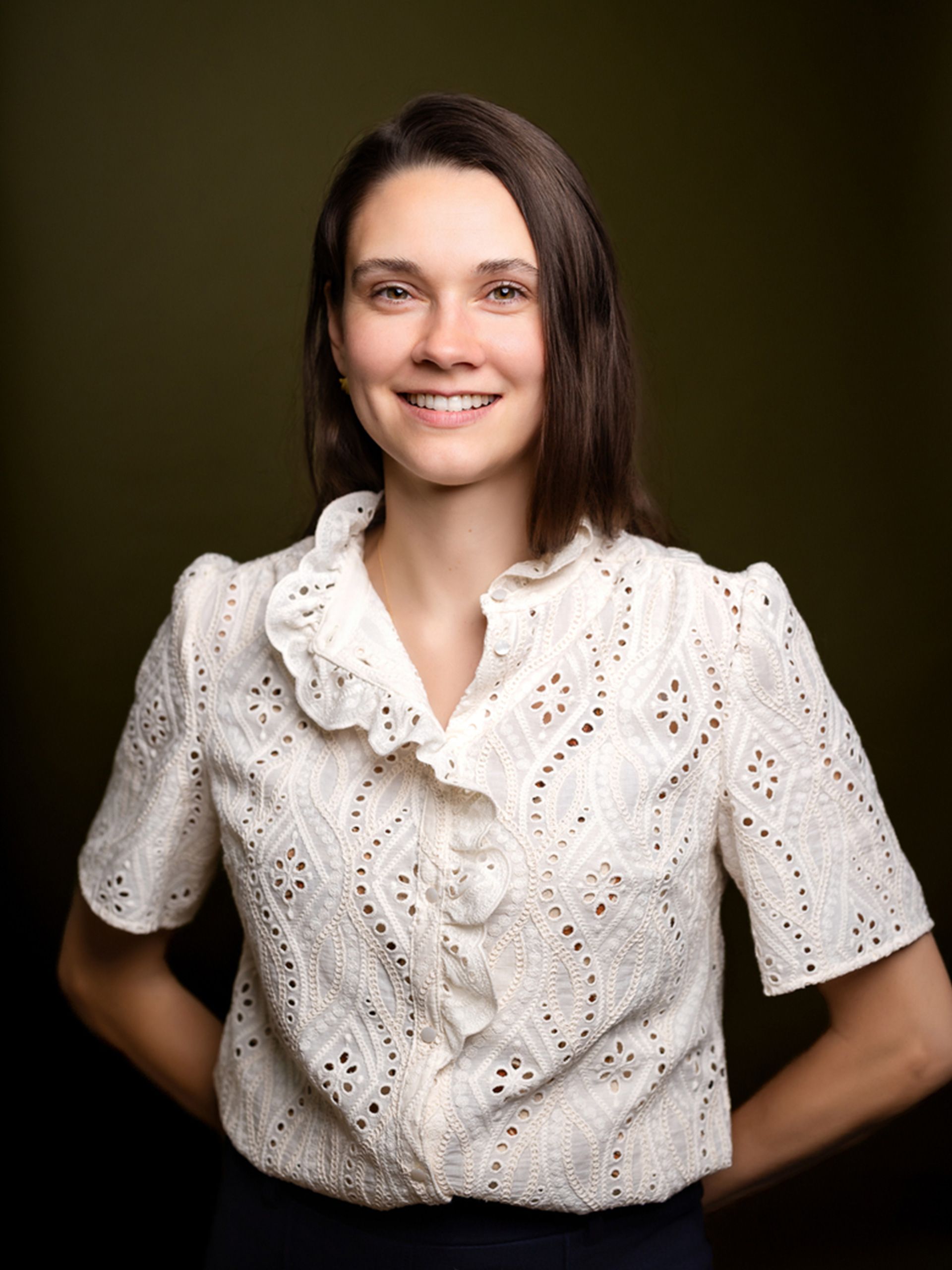 Smiling person in a white blouse against a dark studio background