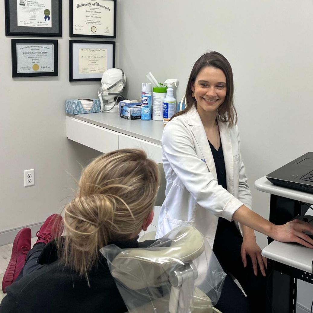 Dentist in white coat smiling at seated patient during a dental exam in a clinic room