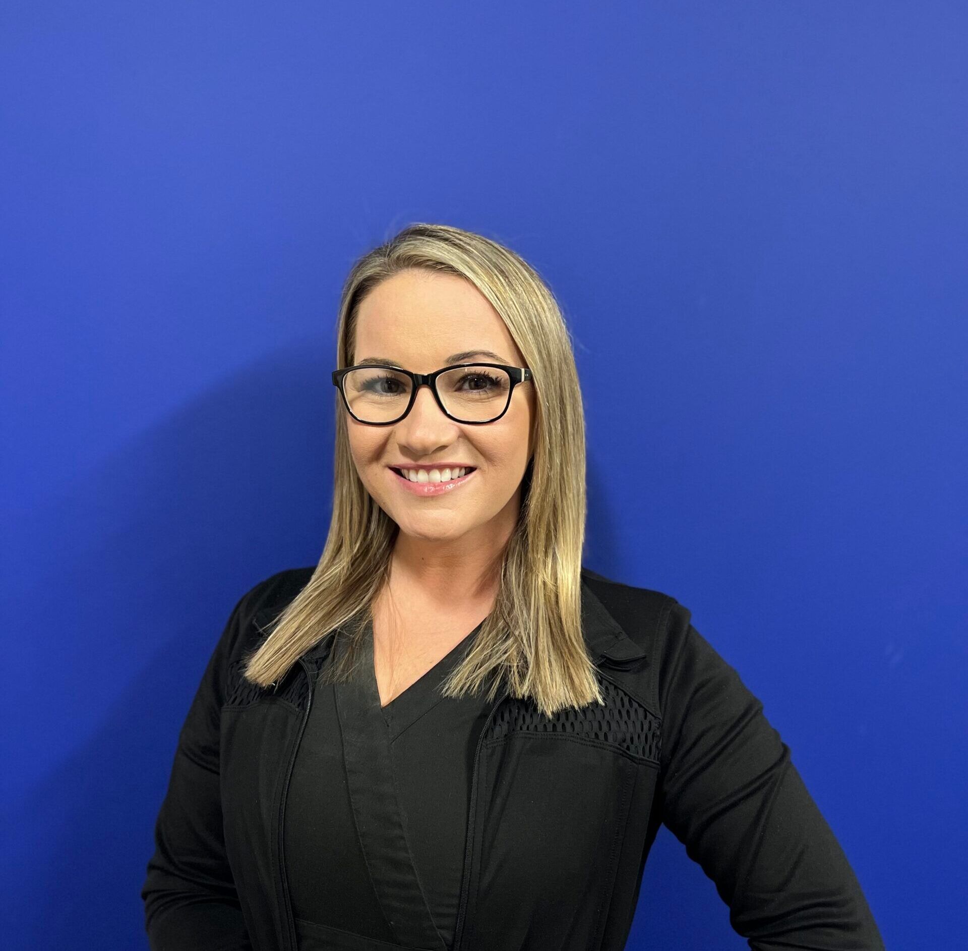 Woman with glasses smiling against a bright blue background