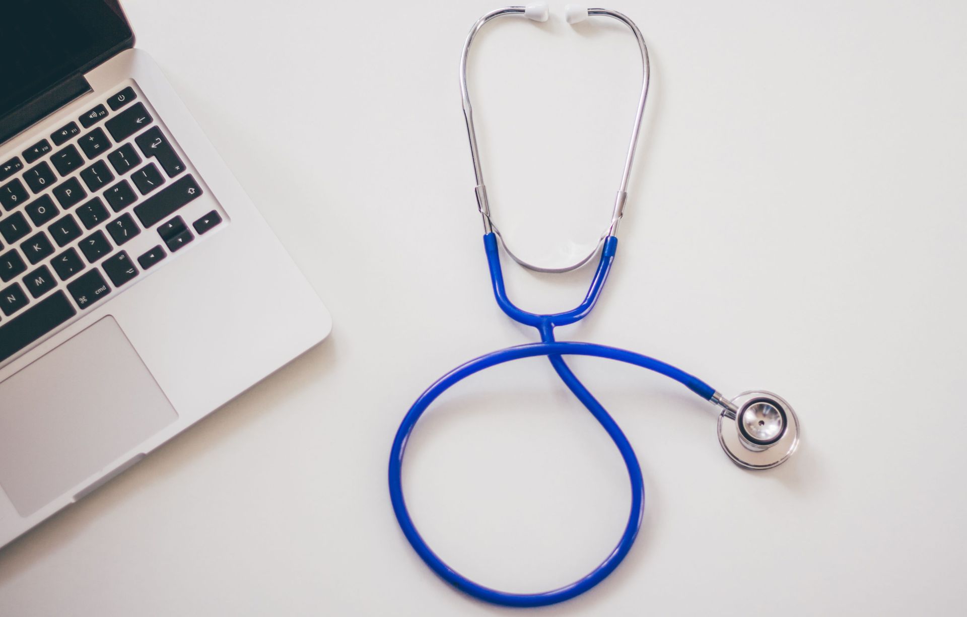 Laptop corner beside blue stethoscope on a white desk