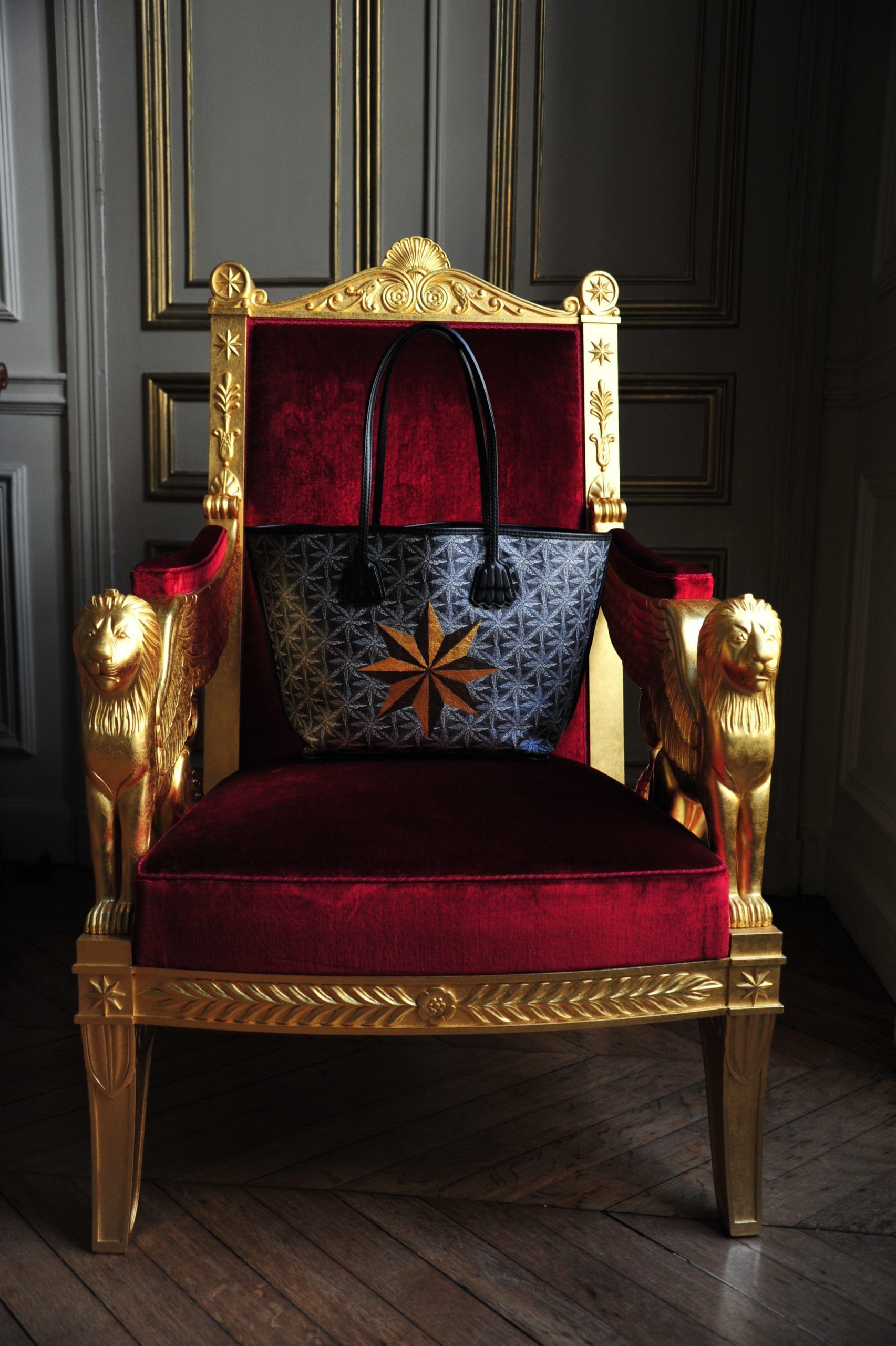 A black embroidered bag on a red velvet chair with gold armrests