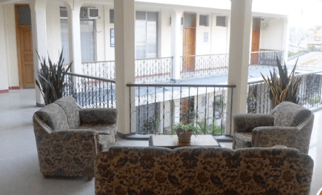 Zona de estar con sillas estampadas y sofá con vistas a un patio desde un pasillo con balcón.
