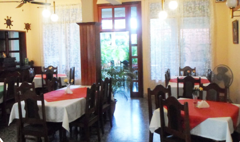 Acogedor comedor de restaurante con manteles rojos y blancos, sillas de madera y una luminosa entrada con ventanales.
