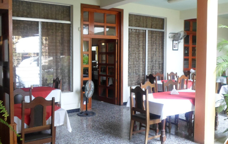 El restaurante cuenta con mesas en el interior, manteles rojos y blancos, sillas de madera y grandes ventanales