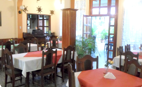 Comedor luminoso con mesas de madera, manteles rojos, sillas y grandes ventanales con vistas a la vegetación.