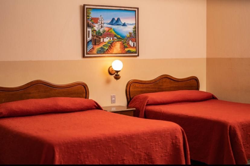 Dos camas rojas impecablemente hechas en una habitación de hotel de tonos cálidos, con un cuadro enmarcado