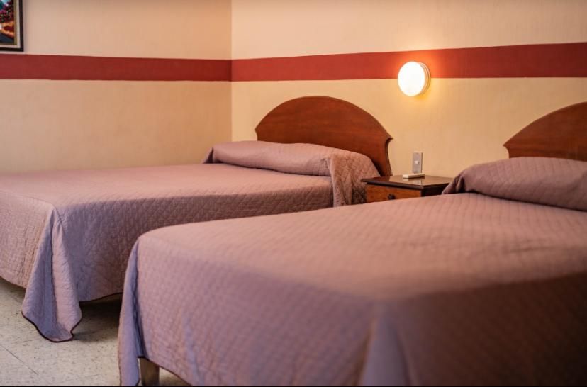 Dos camas impecablemente hechas en una habitación de hotel beige con cabeceros marrones y apliques de pared.