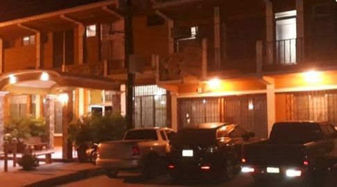 Vista nocturna de un motel con balcones iluminados y coches aparcados delante.
