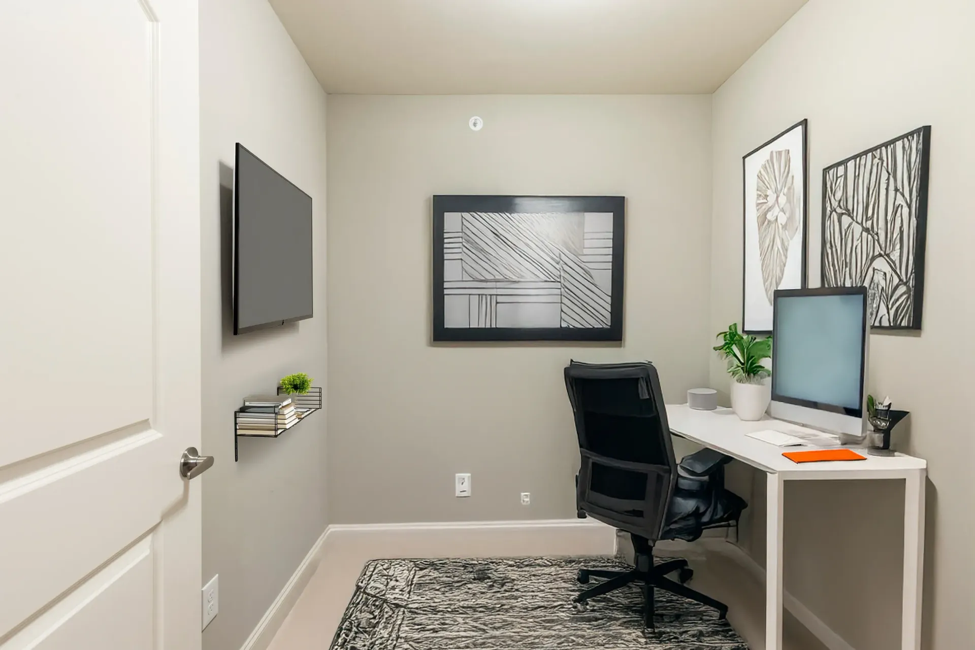 Small apartment home office with a white desk, black ergonomic chair, monitor, plant, rug, and wall art.