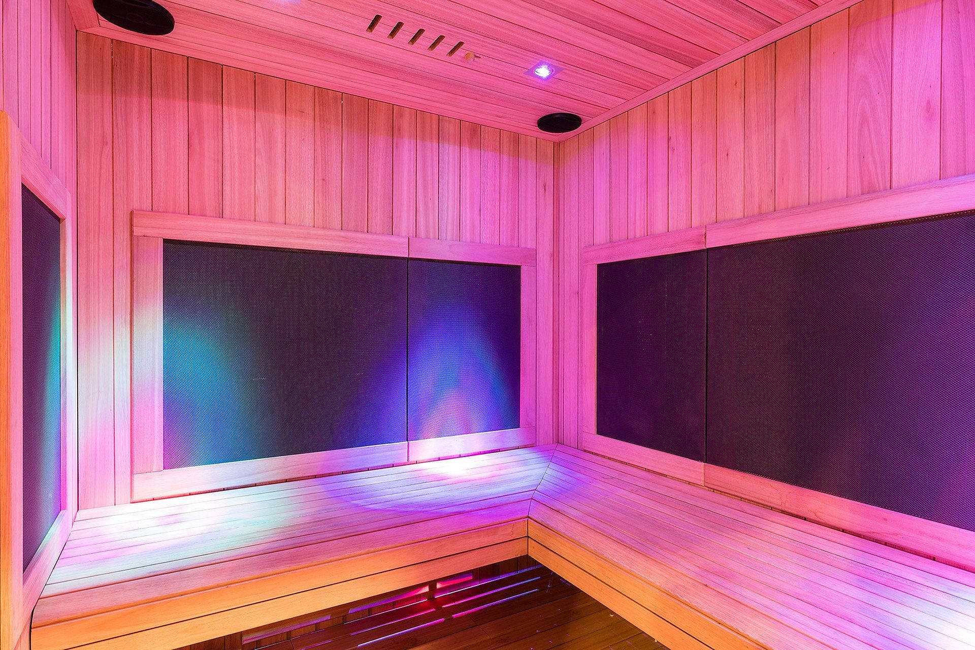 Wood-paneled sauna interior with pink and blue LED lighting and bench seating