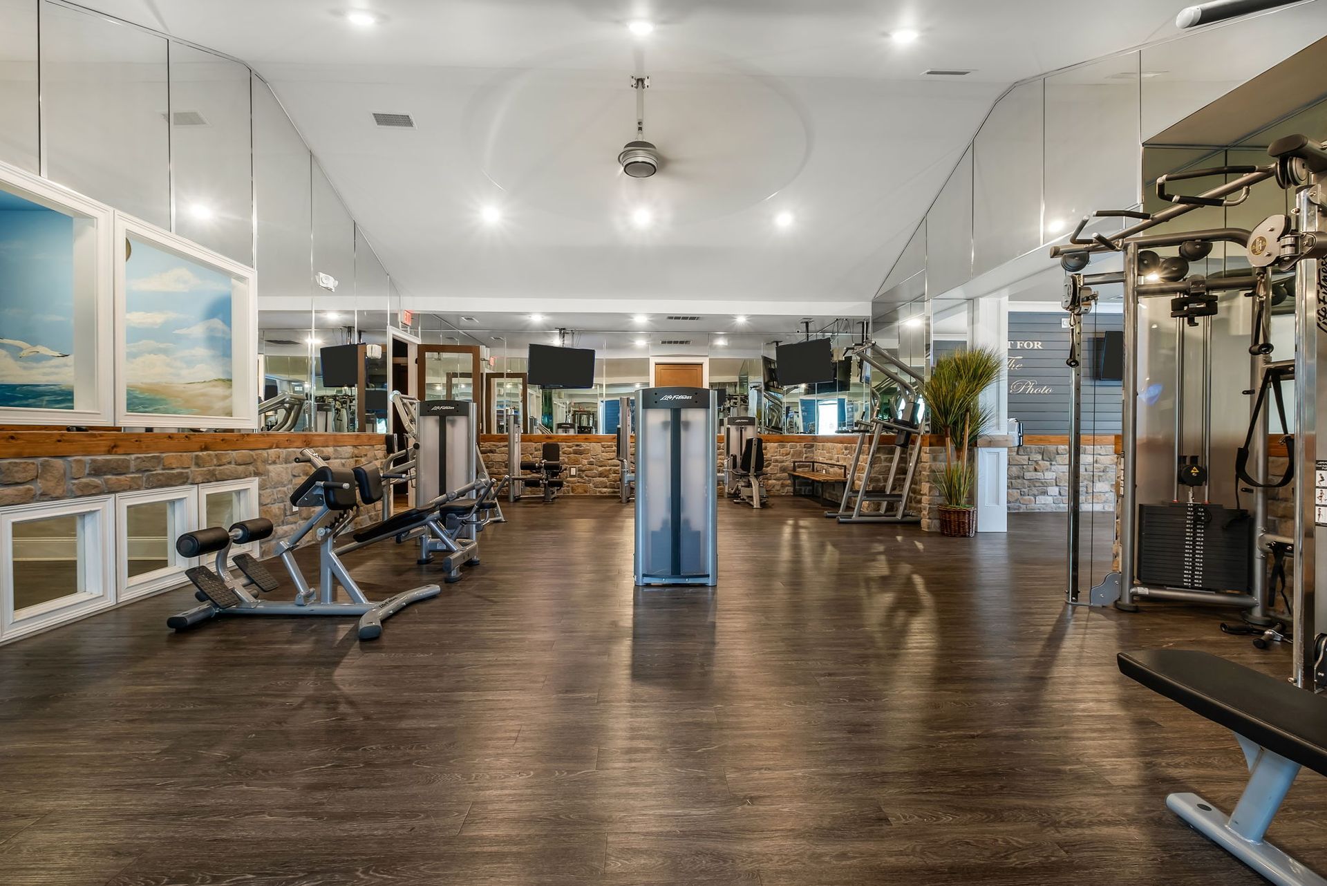 Bright gym with multiple workout machines, equipment, mirrors.