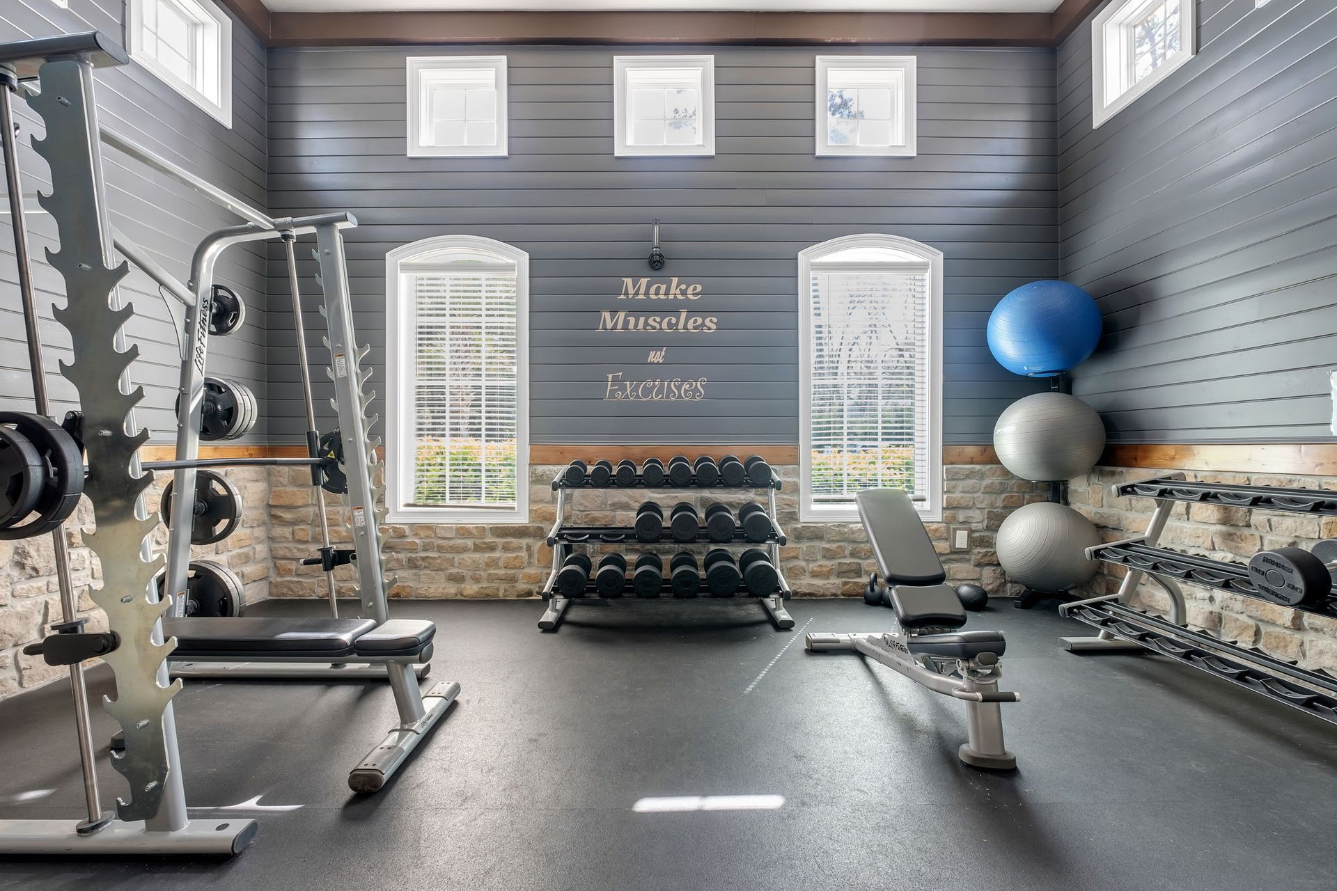 Indoor fitness room with a squat rack, benches, and dumbbells against paneled blue walls.