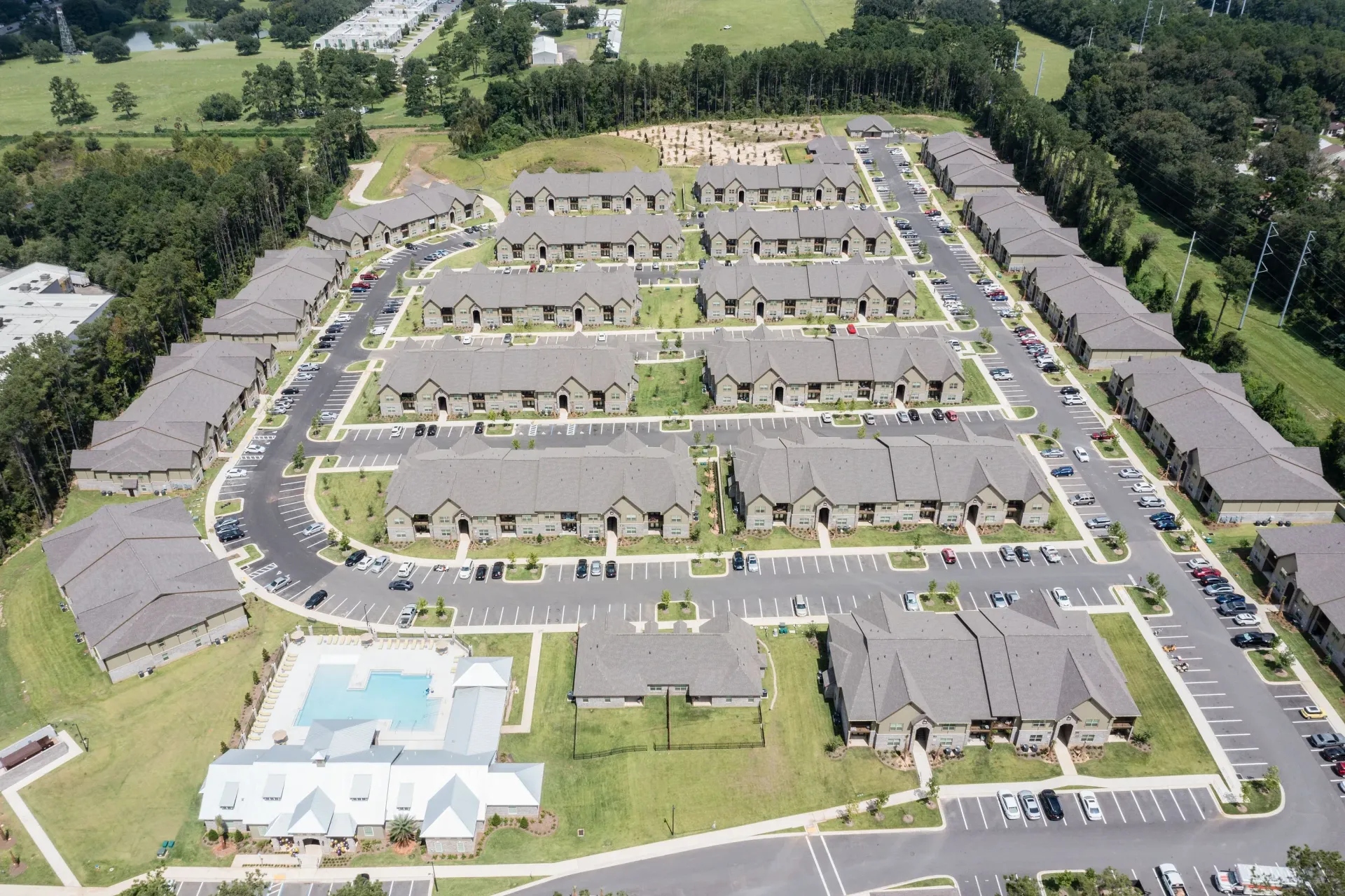 Aerial view of a large apartment complex with multiple buildings, parking, and a central pool.