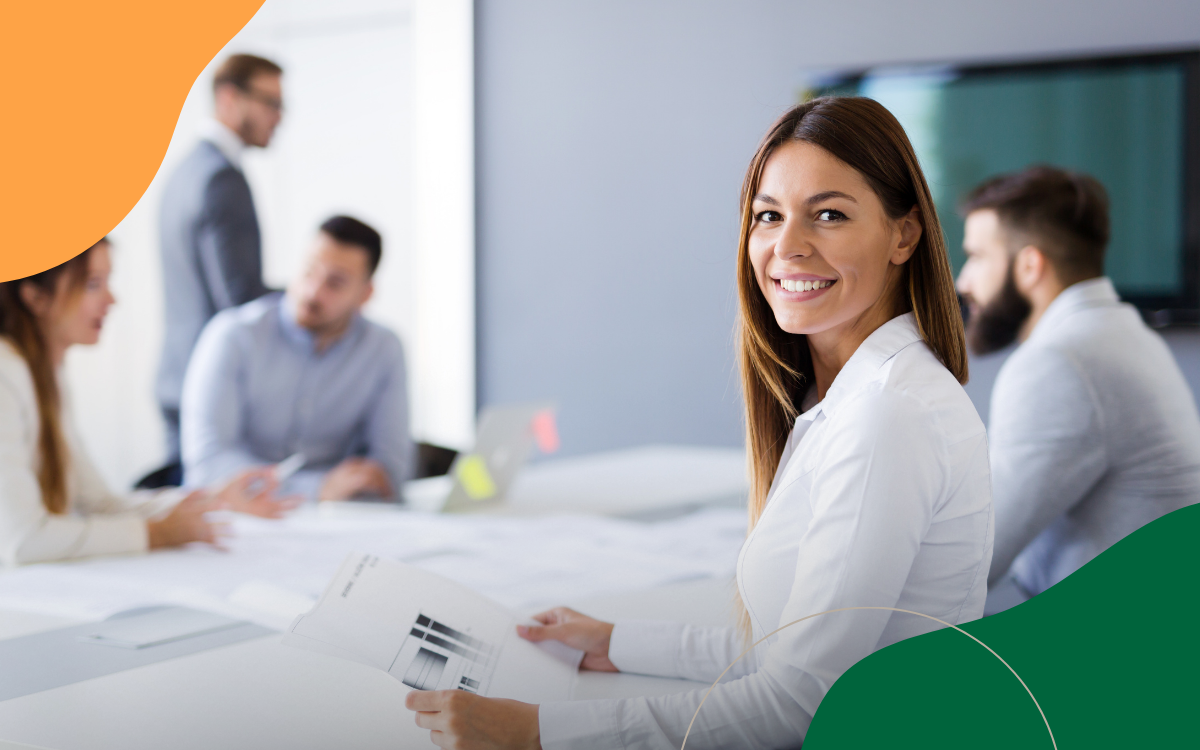 Smiling woman in a white shirt at a meeting table with coworkers in a bright office