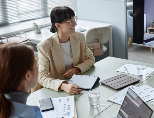 Three people in a bright office meeting around a glass table with laptops and documents