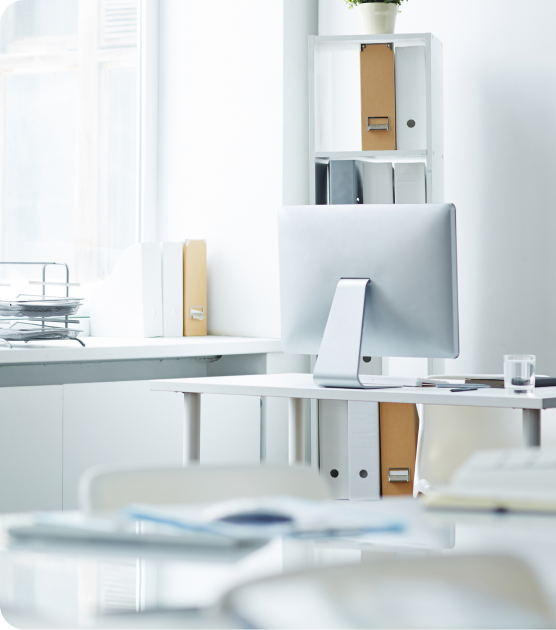 Bright minimalist office with a white desk, computer monitor, shelves, and soft natural light