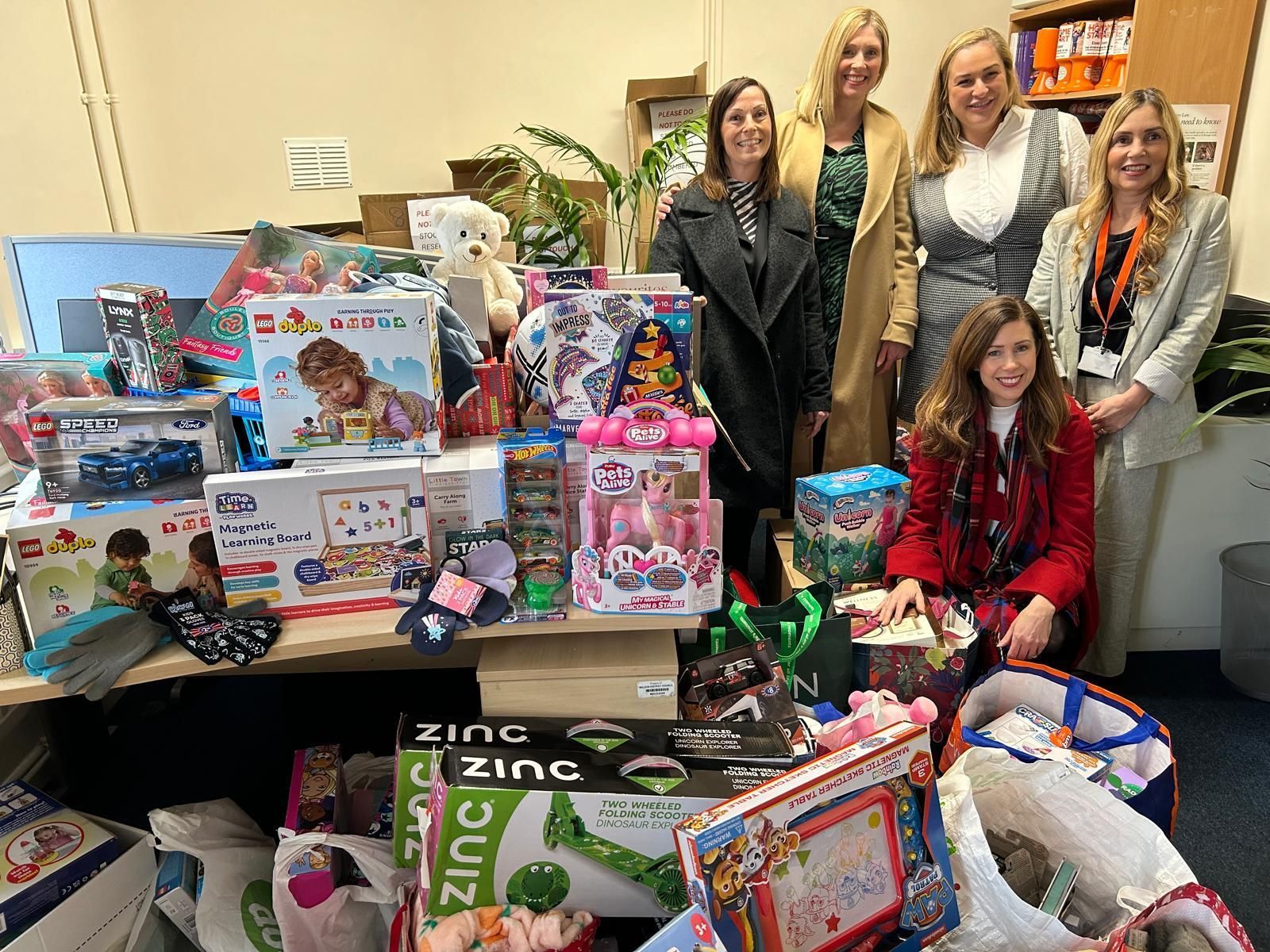 Group posing behind a table of donated toys and gift boxes in an indoor room