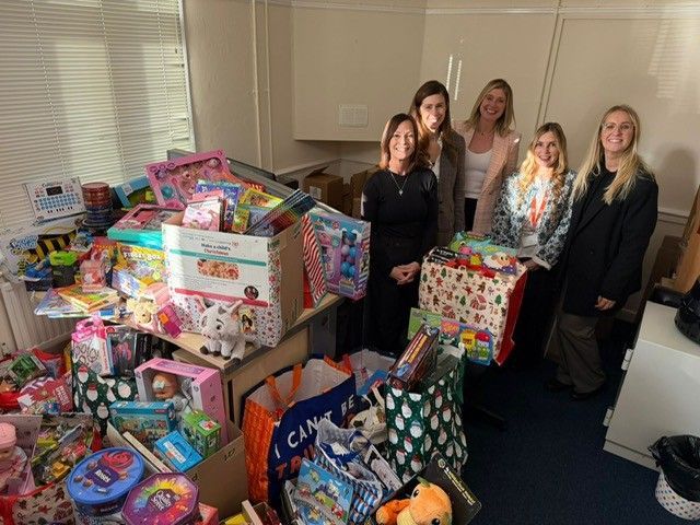 People standing beside a large pile of colorful donated toys and gift boxes indoors