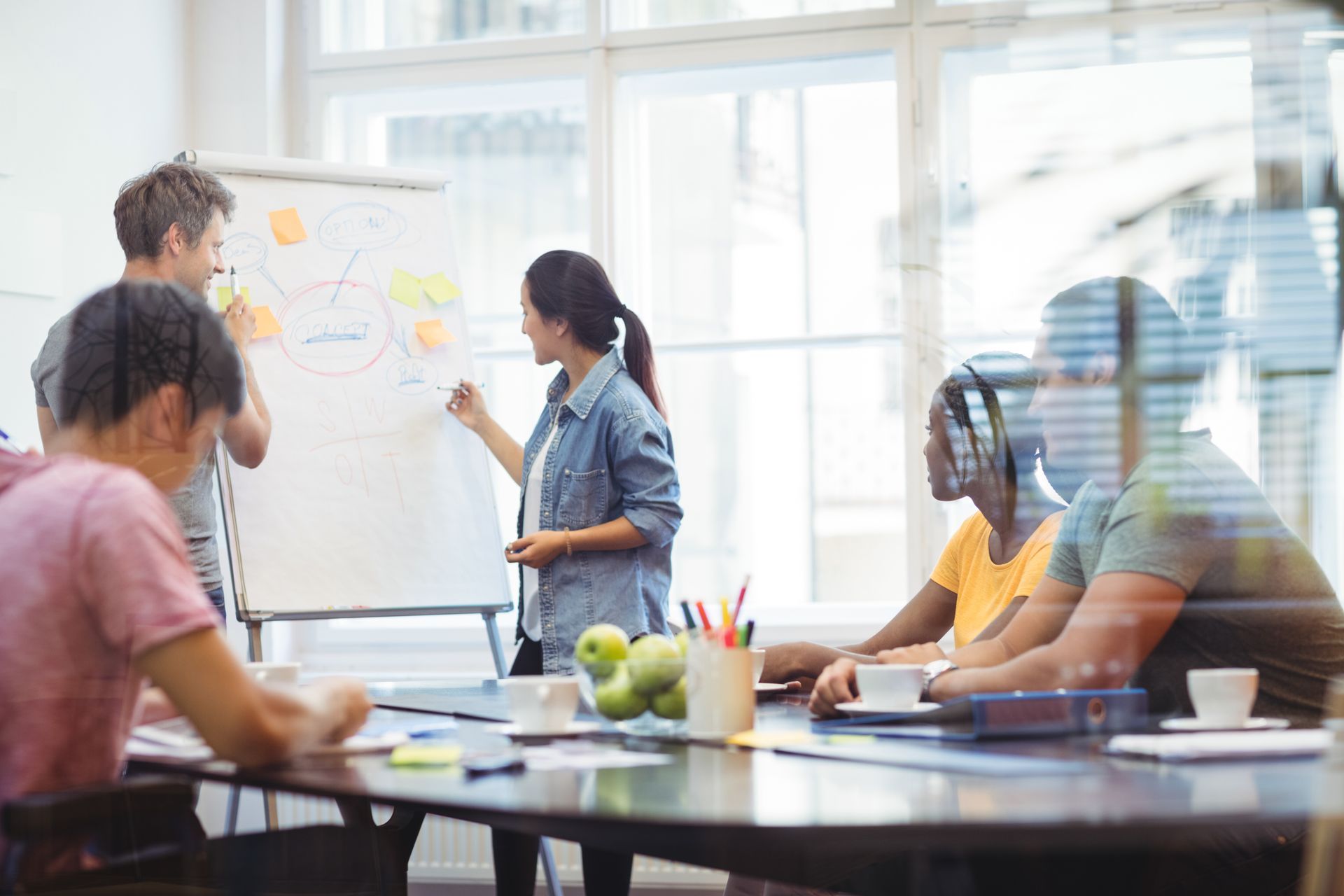 Team meeting in a bright office, with people discussing ideas at a whiteboard and around a conference table