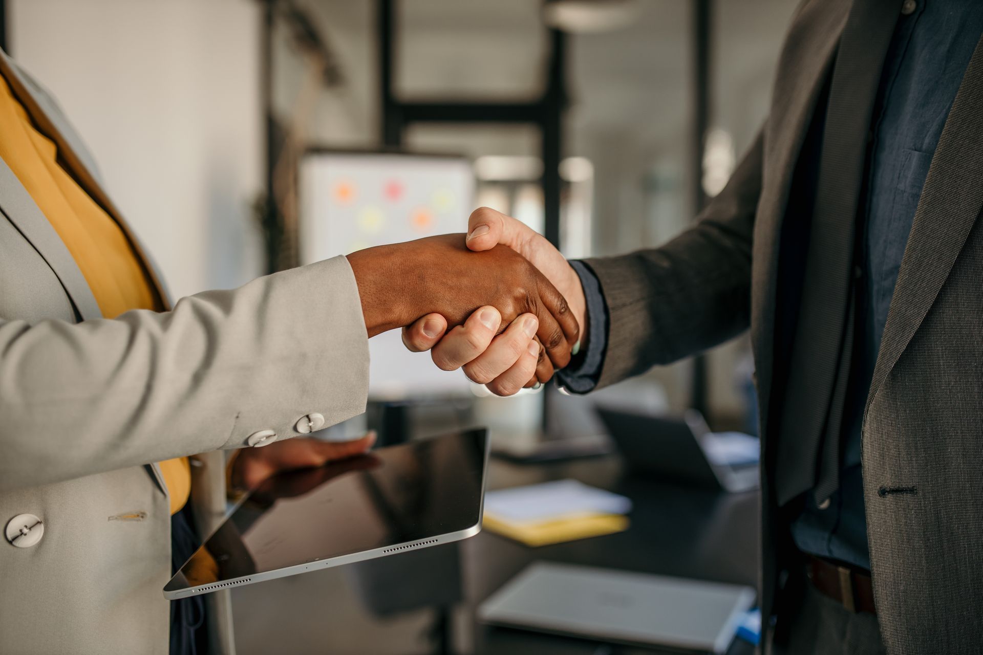 Two people in business attire shaking hands in an office.