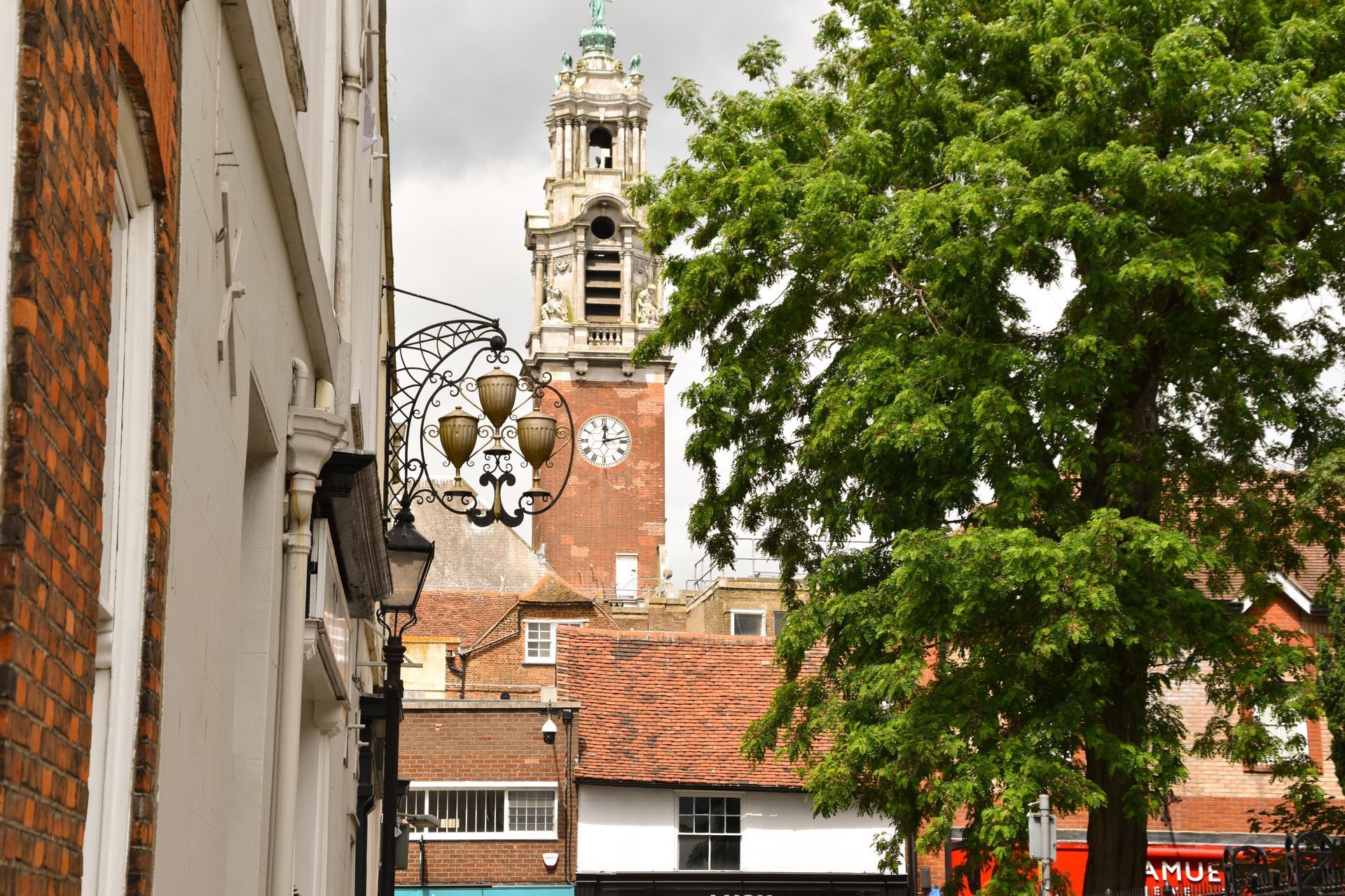 Narrow street with old brick buildings, leafy tree, and a church tower in the background