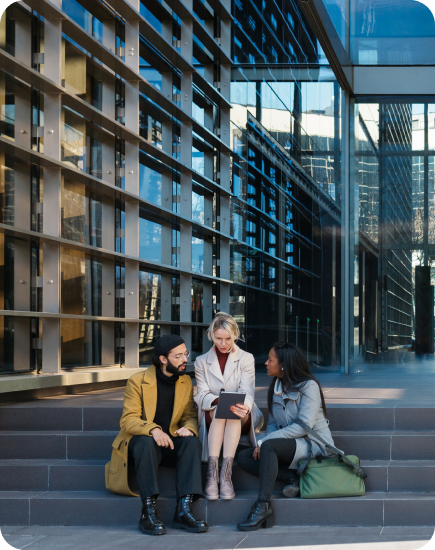 Three people sitting on steps outside a modern glass building, talking together.