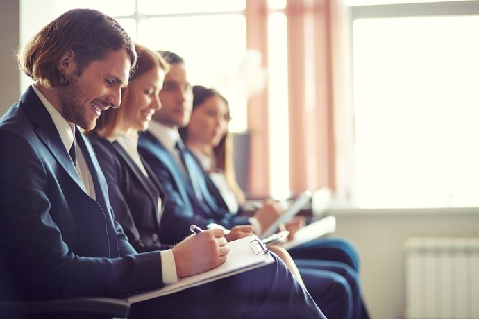 People seated in a row taking notes during a meeting or class in a bright room