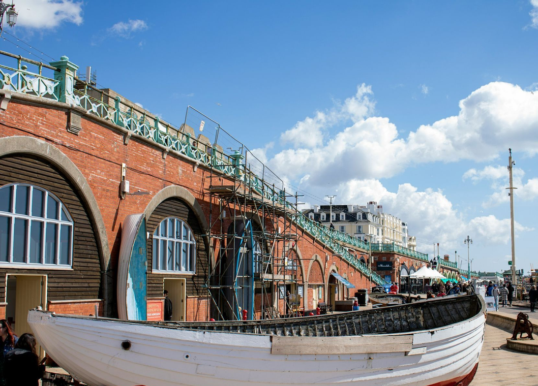 White boat beside red brick arches on a sunny waterfront promenade under a blue sky