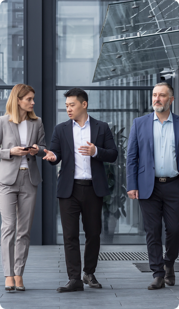 Three businesspeople walking outside a glass office building, talking together.