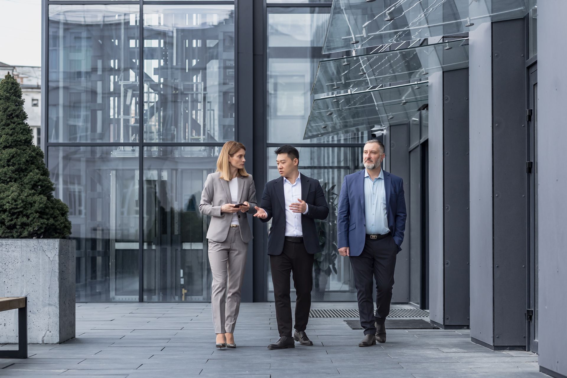 Three business professionals walking and talking outside a glass office building.