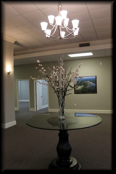 A large round table with flowers under a chandelier. Doors and a landscape picture are in the background.