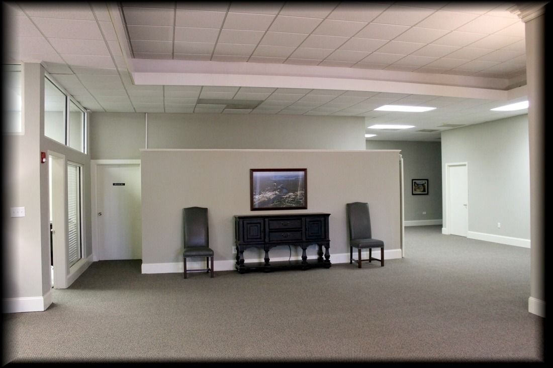 An empty, carpeted room with light gray walls, a cabinet, and two chairs.