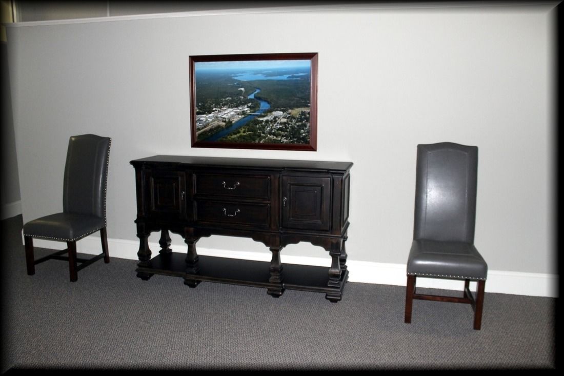 Two gray chairs flank a dark wooden sideboard under a framed landscape photo on a gray wall.